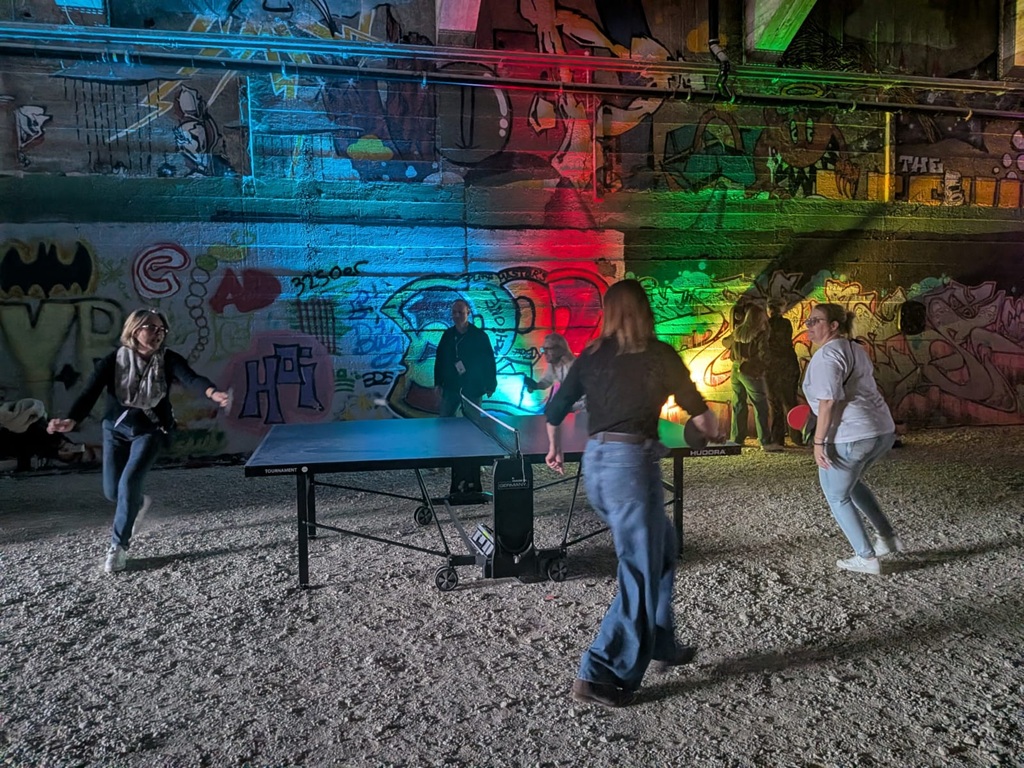 4 personen spielen rundlauf an einem tischtennistisch in einem bunt beleuchtetem tunnel.