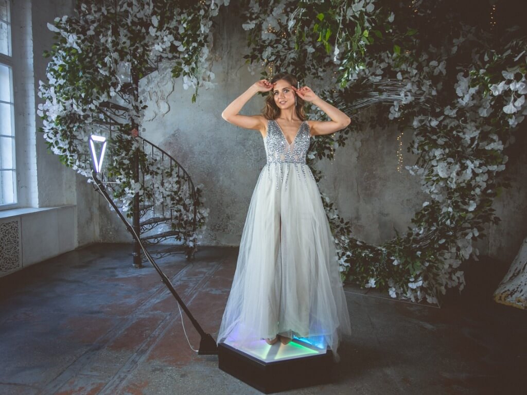 Model in einem langen, eleganten Kleid steht auf der beleuchteten Plattform der 360 Grad Fotobox.