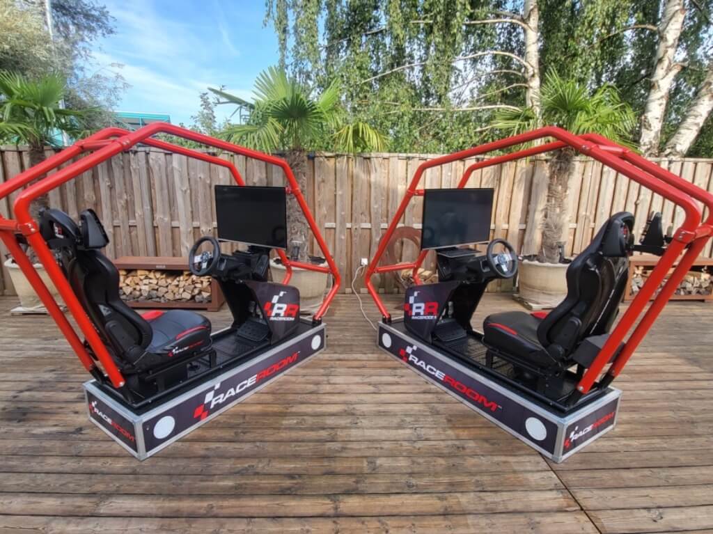 Drei gebrauchte Raceroom Rennsimulatoren mit roten Überrollbügeln und großen Bildschirmen stehen auf Holzterrasse.