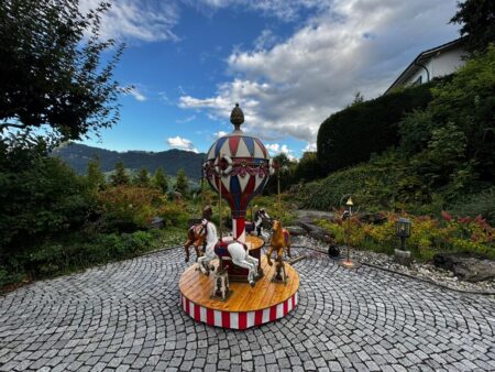 ballon karussell mit 4 pferden auf einem pflasterboden. im hintergrund eine tolle aussicht auf berge.