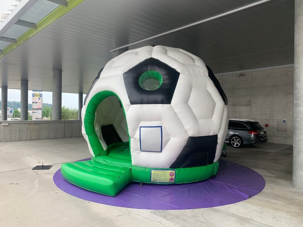 Aufblasbare Hüpfburg in Form eines großen Fußball-Domes mit grünem Eingang und Dach.