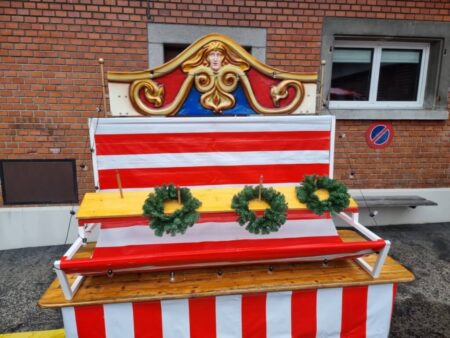 Spielstandort mit drei grünen Adventskränzen auf Stäben vor rot-weiß gestreiftem Hintergrund
