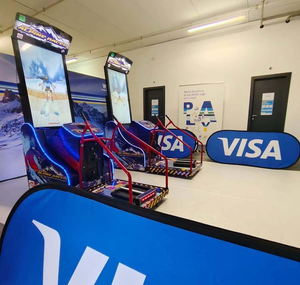 2 alpine racer skisimulatoren nebeneinander. led beleuchtet, auf dem bildschirm ein rennspiel.im hintergrund werbefahenn von visa.