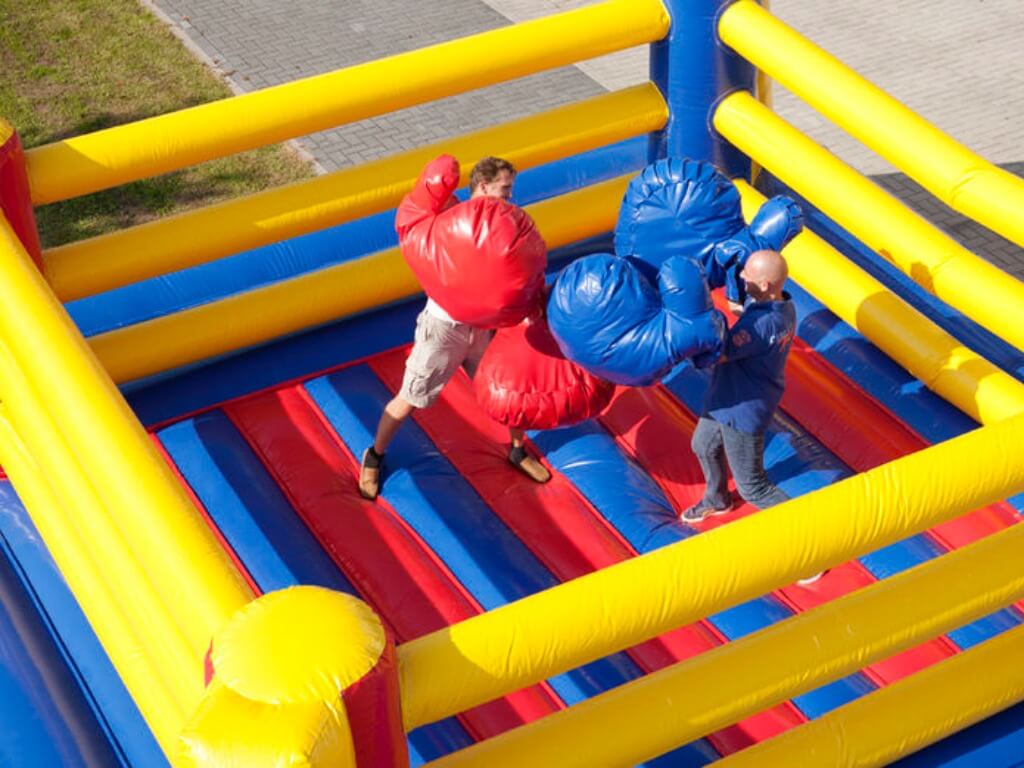 Zwei Männer boxen mit überdimensionalen Handschuhen in einem gelb-blau-roten aufblasbaren Boxring.