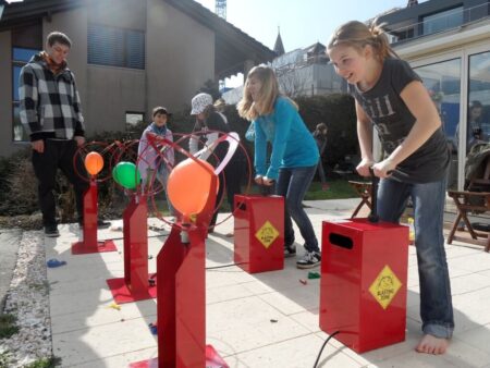 Zwei Kinder pumpen an roten Ballon Blaster Maschinen im Wettkampf um den Luftballon zum Platzen zu bringen.