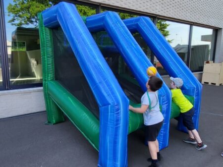 Zwei Kinder spielen an einer aufblasbaren Basketball-Challenge und werfen Bälle in die Körbe.