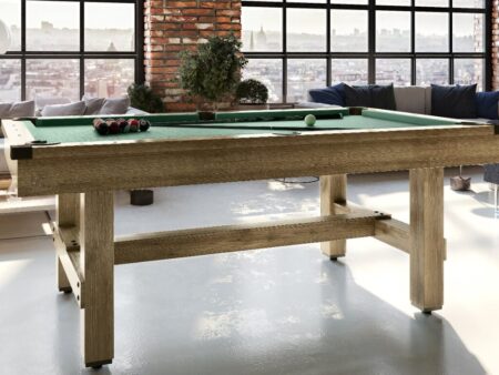 Robuster Billardtisch mit grünem Spielfeld in einem hellen Loft mit Ziegelwand und großer Fensterfront.