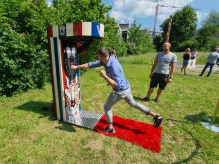 Mann schlägt kräftig auf den Boxautomat Nostalgia bei sonnigem Wetter auf einer grünen Wiese.