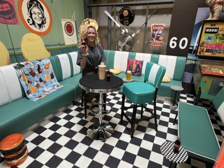 hübsche junge frau sitz in einem diner am stehtisch auf einem barhocker mit einer cola in der hand.