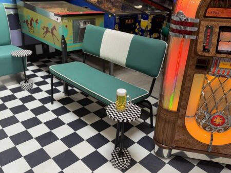 türkis weiss gestreifte diner sitzbank auf schwarz weissem kachelboden. daneben eine beleuchtete jukebox.