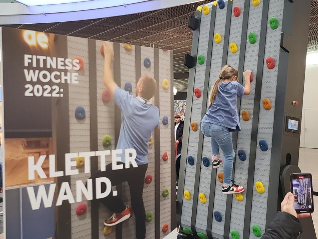 Kind klettert an der Endlos Kletterwand mit bunten Griffen während einer Fitnessveranstaltung.