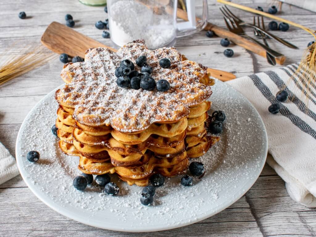 Goldbraune Waffeln auf einem Teller mit Blaubeeren und Puderzucker serviert in rustikaler Holzumgebung