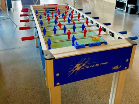 Großer Tischfussball mit sechs Spielerreihen und roten sowie blauen Spielfiguren in modernem Eventraum