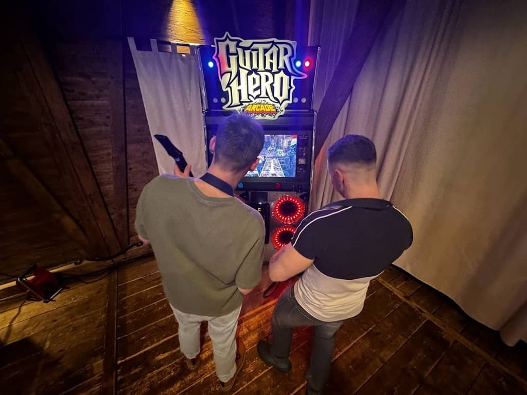 2 prsonen vor der arcade maschine guitar hero mit jeweils einer gitarre in der hand.