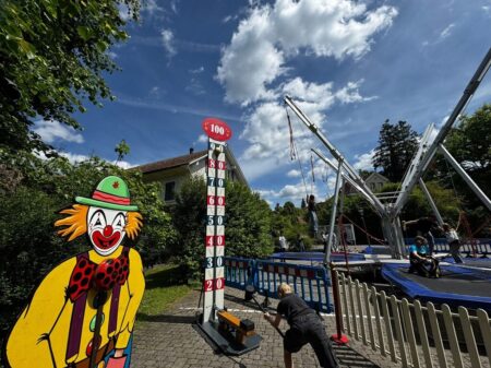 Kind schlägt mit Hammer auf Hau den Lukas Jahrmarktspiel neben farbenfrohem Clown-Standee.