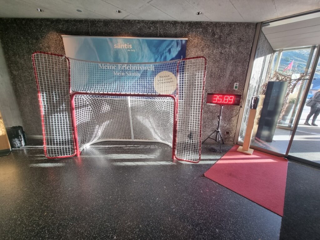 Hockeytor mit Netz vor Werbetafel und digitaler Tafel zeigt gemessene Schussgeschwindigkeit an.