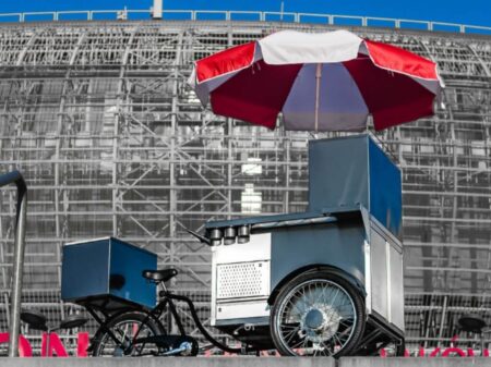 Hot Dog Fahrrad mit großem roten und weißen Sonnenschirm vor moderner Architektur
