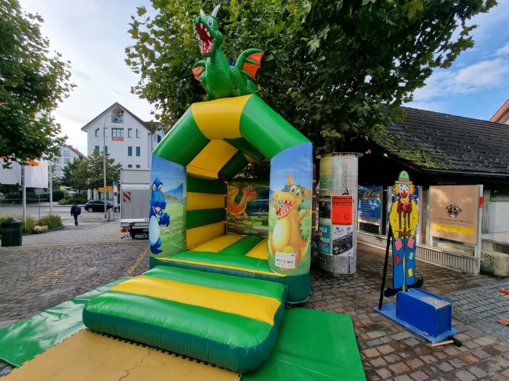 Bunte Hüpfburg Midi mit Dach und Drachenfigur oben, umgeben von Drachenillustrationen auf dem Spielplatz