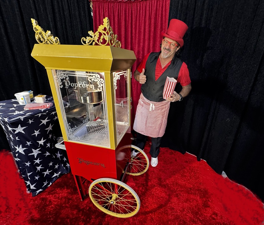 edler clown macht popcorn mit einer nostalgischen maschine auf rotem teppich vor rot schwarzem vorhang.