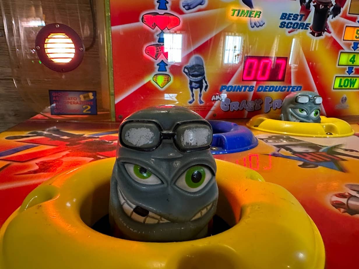 Froschkopf kuckt aus dem Loch eines Hammer Schlag Spielautomaten.