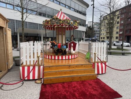 achönes zkinderkarussell auf einem marktplatz. roter teppich vor der treppe, rot weisses dach und verschiedene Tierfiguren auf dem Karussell.