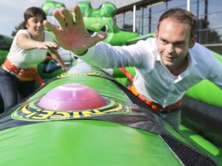 Zwei Personen in Sicherheitsgurten kämpfen auf einem grünen Bungee Run gegeneinander.
