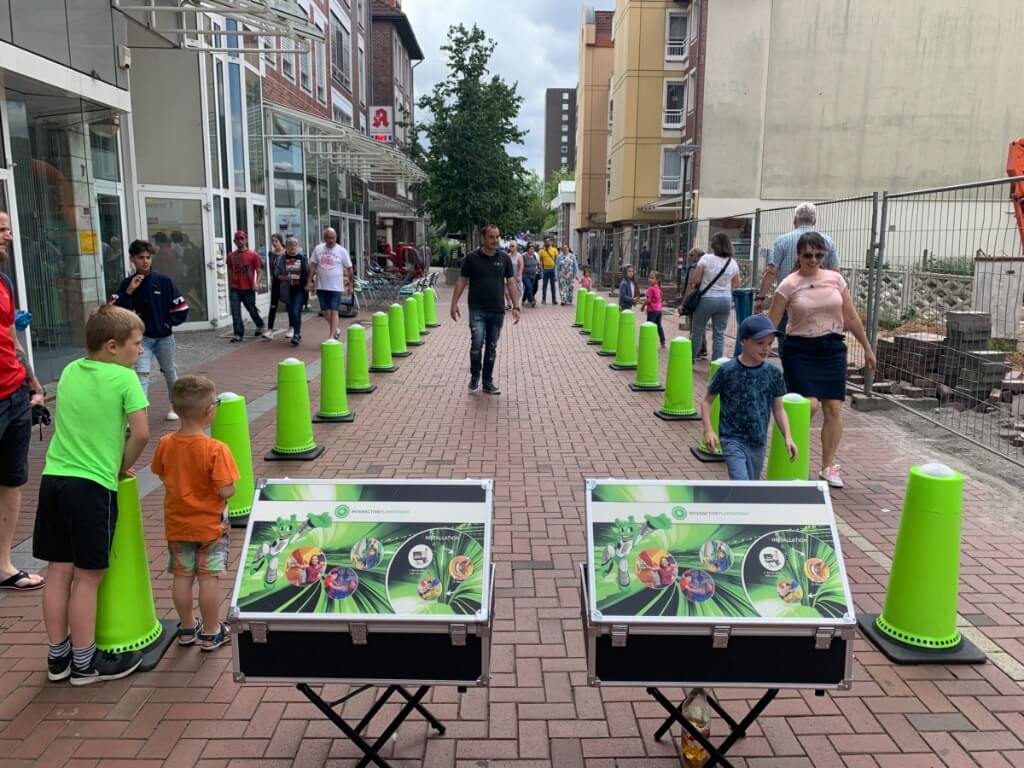 Kinder und Erwachsene spielen das interaktive Pylonen-Reaktionsspiel mit leuchtenden grünen Pylonen auf einem Fußweg in der Stadt.