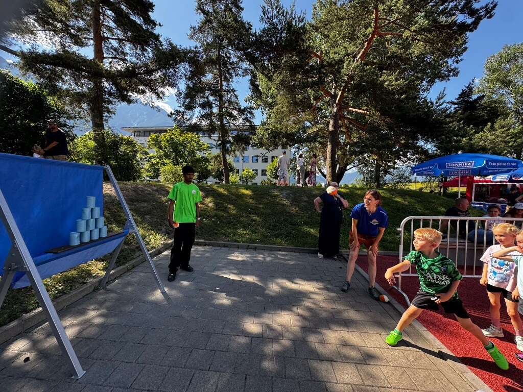 Dosenwerfen-Stand mit blauer Rückwand und buntem Auffangtuch, betreut von Erwachsenen, bei Outdoor-Event.