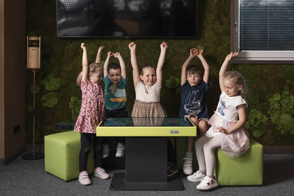 kinder heben die arme hoch und sitzen um den 4touch spieletisch
