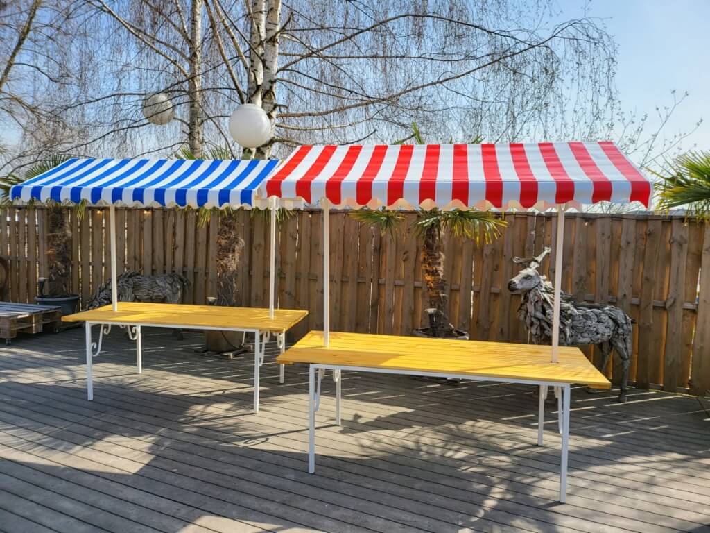 Zwei Marktstände mit blau-weißem und rot-weißem gestreiftem Dach und gelber Arbeitsplatte im Außenbereich