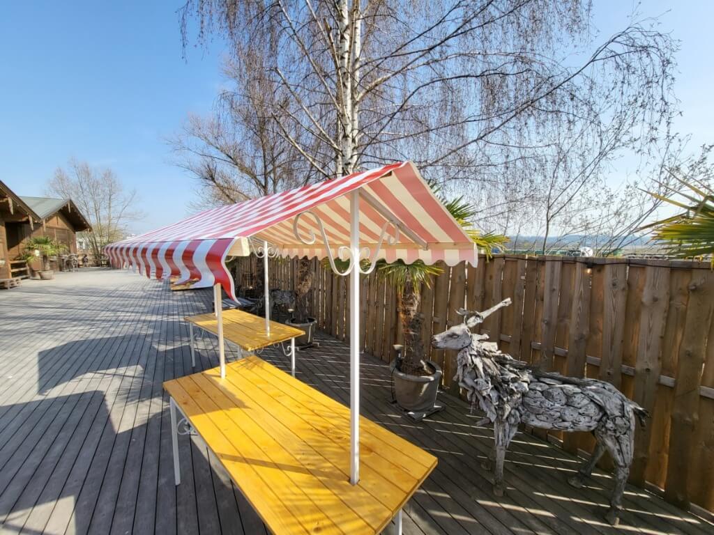 Langer Marktstand mit rot-weiß gestreiftem Dach und robustem Holzunterbau auf Holzterrasse