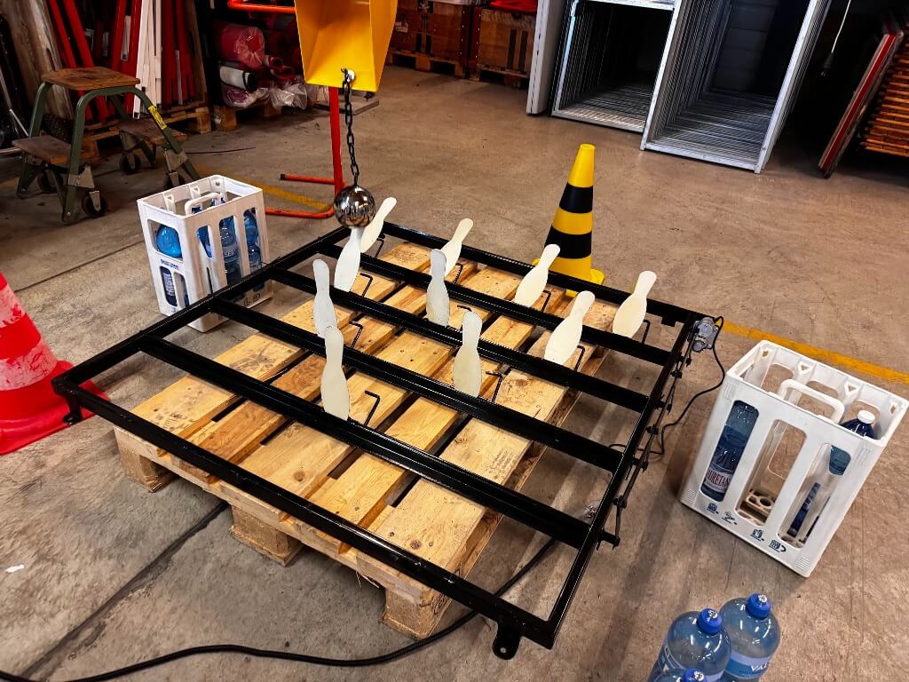 Kinderspiel mit Minibagger-Bowling: Kleine Bowling-Pins und Ball auf einem Holzpallettrahmen im Werkstattbereich