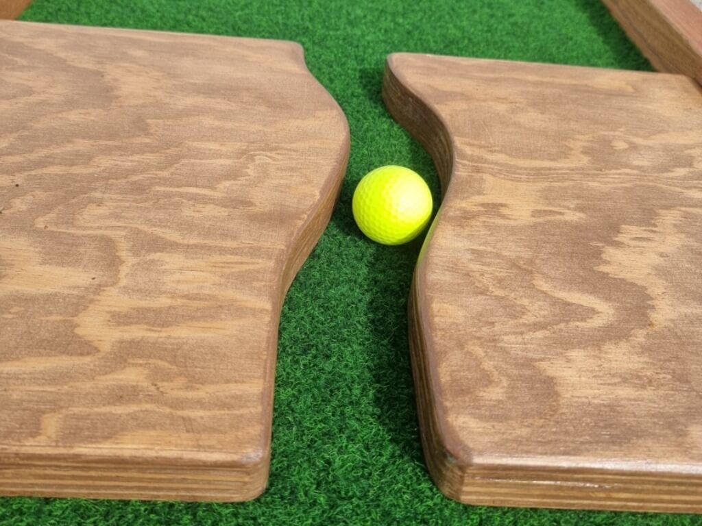 Gelber Minigolfball liegt zwischen zwei Holzhindernissen auf grünem Kunstrasen.