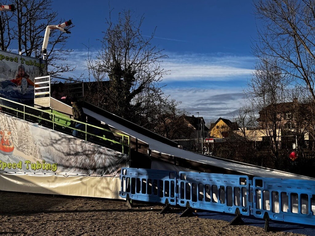 Mobile Tubing-Rodelbahn im Freien mit Bergaufstieg und blauen Absperrungen bei klarem Himmel.