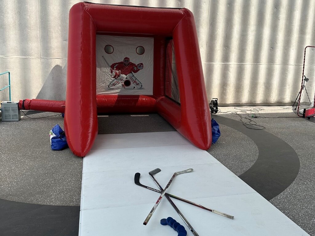 Rotes aufblasbares Hockeytor mit Zielscheibe und drei Hockeyschlägern davor auf glattem Untergrund