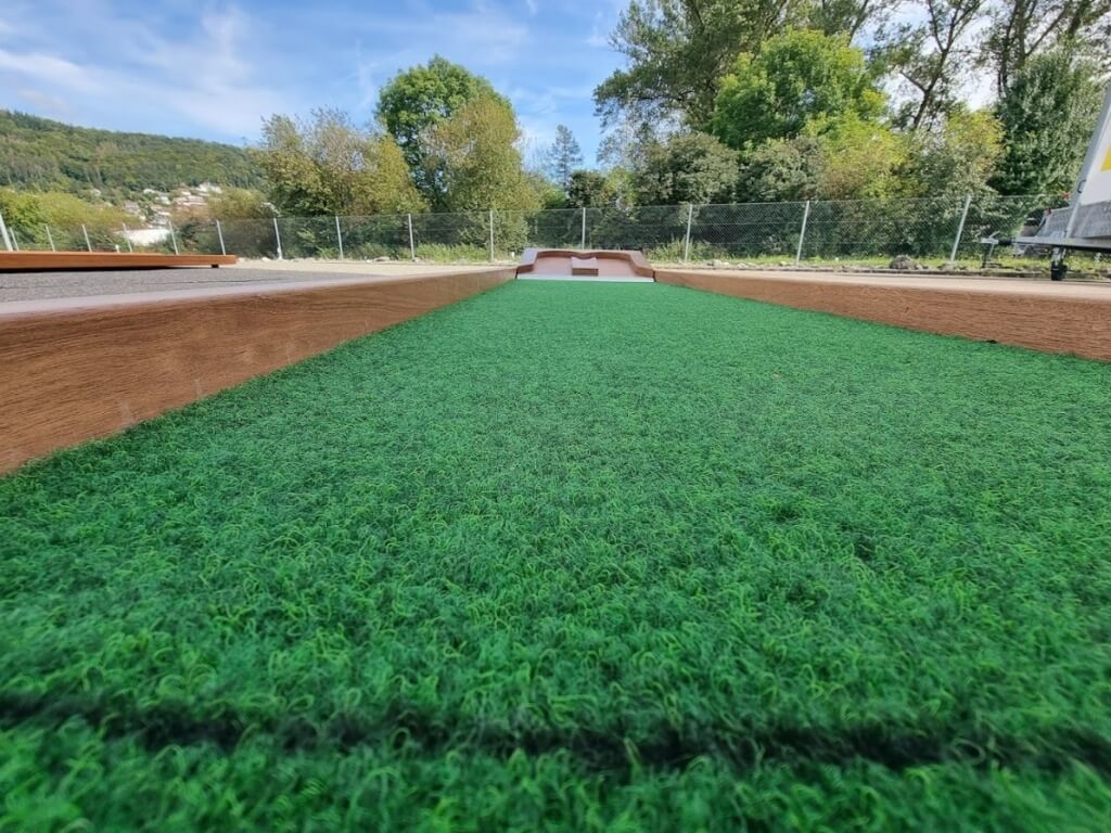 Nahaufnahme einer mobilen Minigolfbahn mit grünem Kunstrasen und Holzeinfassung im Outdoorbereich.