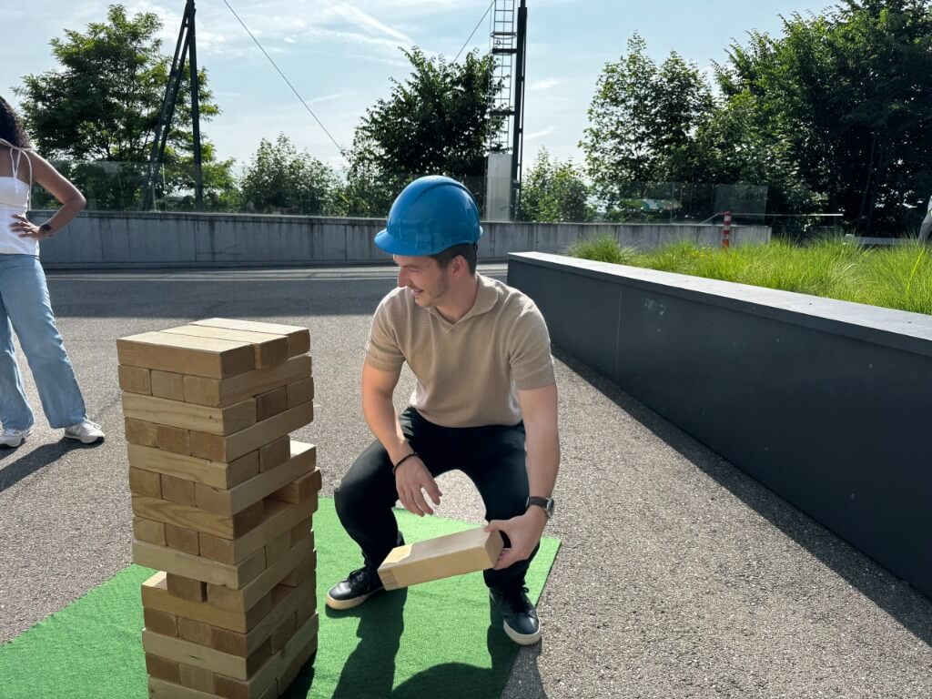 Junger Mann in Freizeitkleidung spielt XXL Jenga im Freien neben hohem Holzturm.