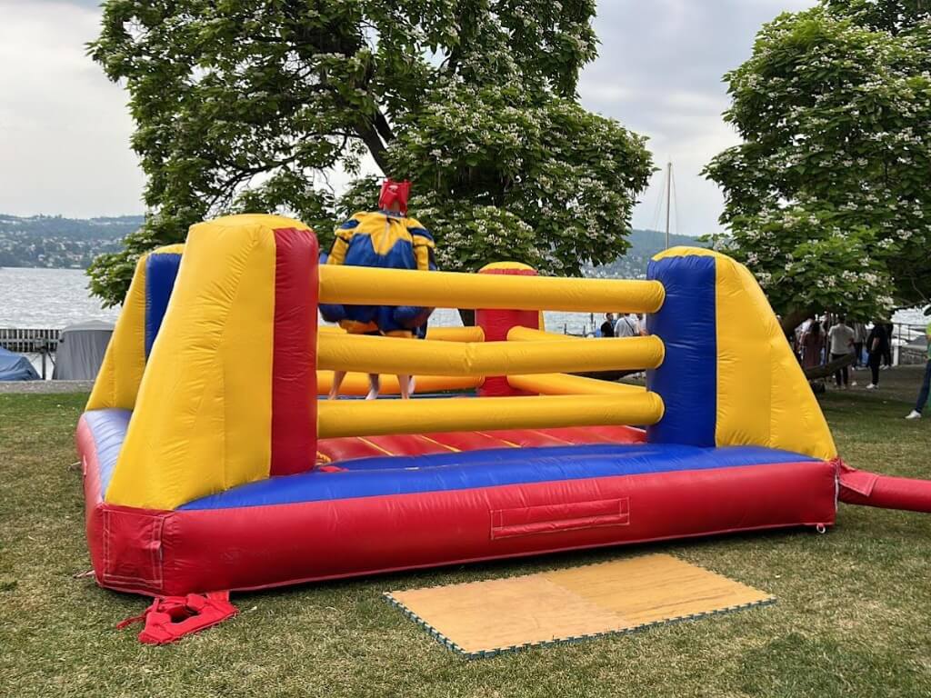 XXL aufblasbarer Boxring mit farbenfrohen Seitenwänden und zwei Spielern mit großen Handschuhen am See