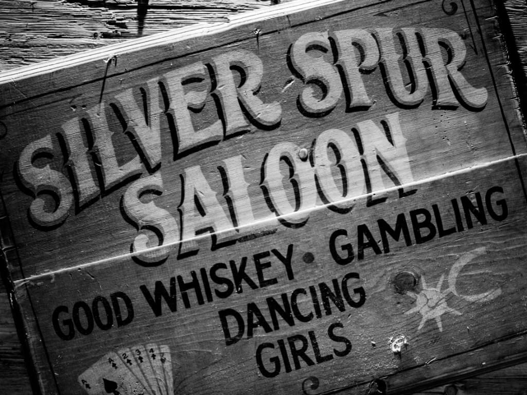 Rustikales Holzschild mit Schriftzug Silver Spur Saloon sowie ergänzenden Texten zu Whiskey, Gambling, Dancing und Girls.