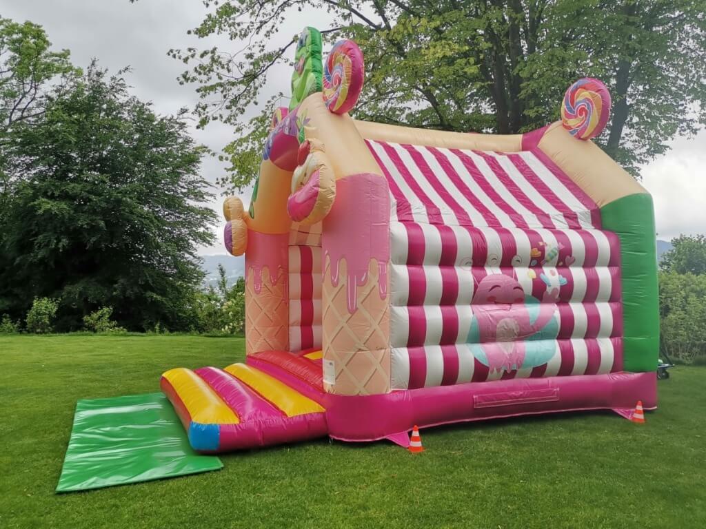 Farbenfrohe 5 Meter lange Hüpfburg im Süssigkeiten-Design mit Dach steht auf grüner Wiese.