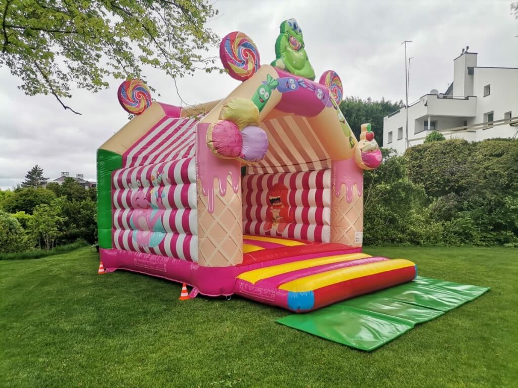 Bunte Hüpfburg mit Süssigkeiten-Motiv auf einer grünen Wiese unter bewölktem Himmel