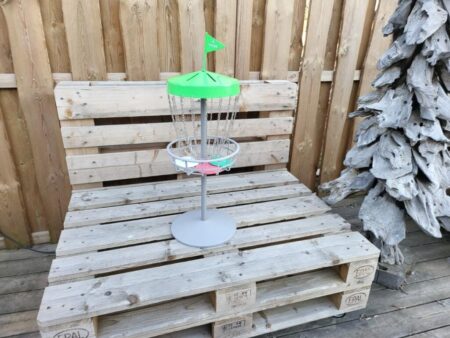 Tragbarer Mini Disc Golf Fangkorb mit grünem Dach steht auf Holzpalette vor Holzzaun