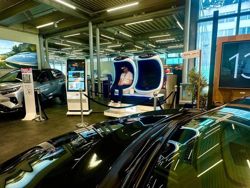 Das VR Cinema steht in einem Autohaus umgeben von Autos. Eine Person spielt gerade.