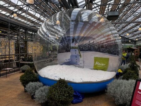 Riesige aufblasbare Schneekugel mit künstlichem Schnee und Schneemann-Dekoration in einem großen Wintergarten.