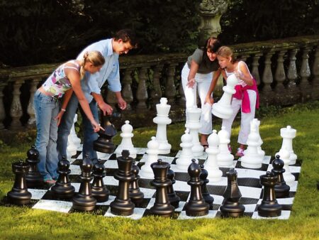 Vier Personen spielen zusammen ein lebensgroßes Gartenschachspiel auf einer Wiese.