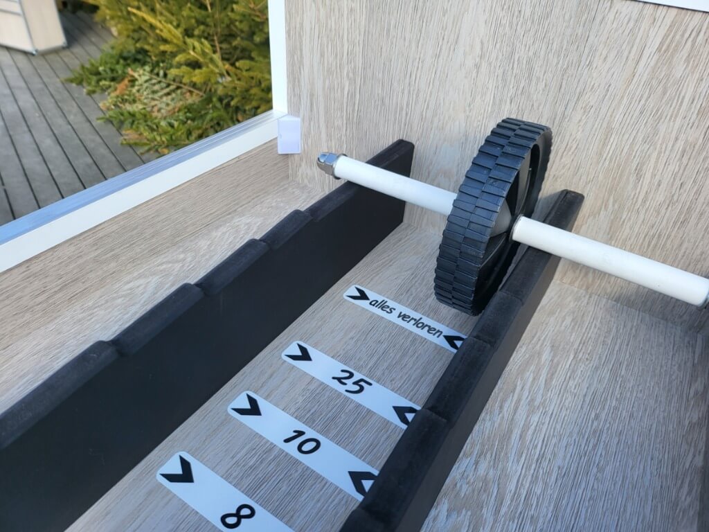 Zahlenroller-Holzspiel mit schwarzem Rad auf weißem Griff in Spielfeld mit Punktwerten und Regelmarkierung